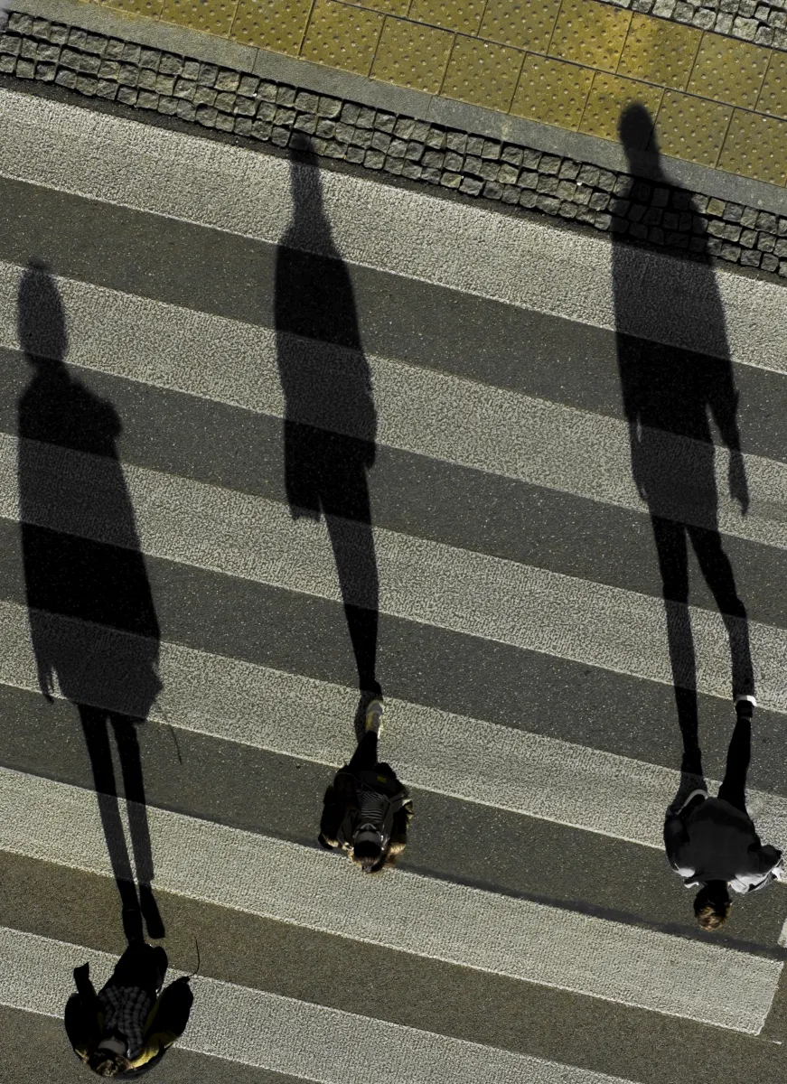 Three elongated pedestrian shadows crossing a zebra crossing